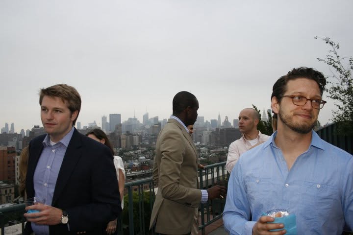 Business professionals talking at a rooftop networking event with a city skyline behind them
