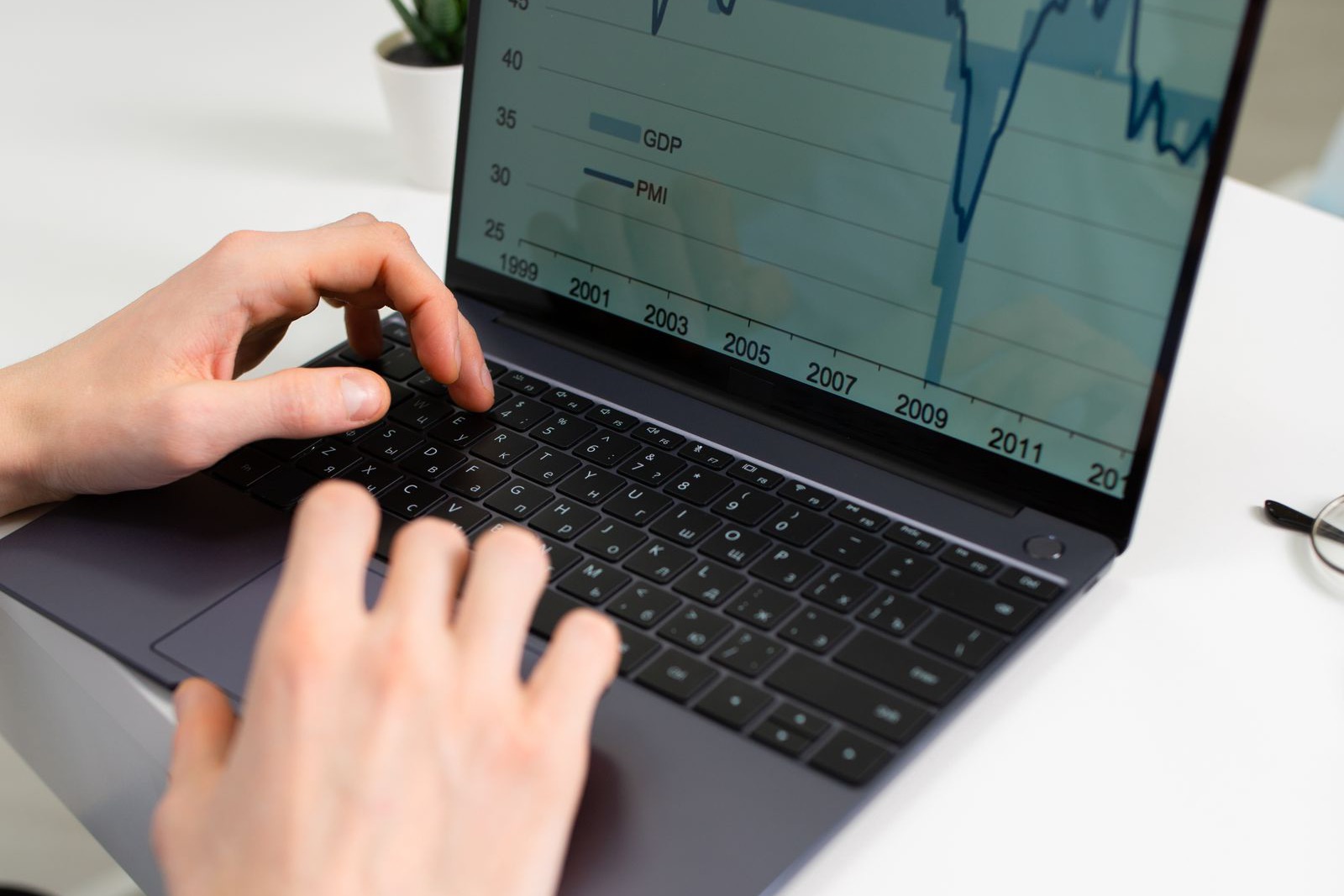 Hands typing on a laptop keyboard while a GDP and PMI line chart is open on the screen
